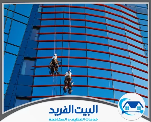 تركيب واجهات زجاج في الشارقة 0567627005 شركة البيت الفريد فنيان يتدليان بالحبال لتنظيف واجهة زجاجية زرقاء مزينة بخطوط حمراء بارزة تحت أشعة الشمس